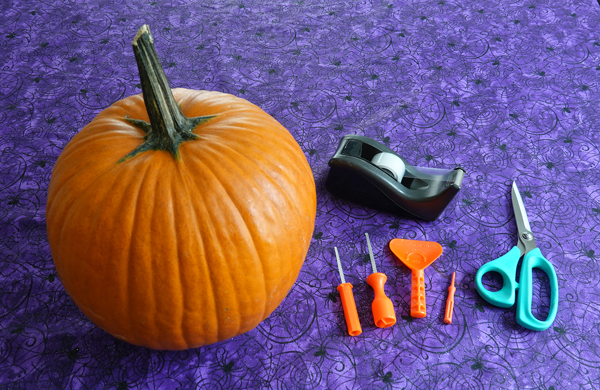 A pumpkin, a tape dispenser, Pumpkin Masters carving tools and scissors laid out for carving